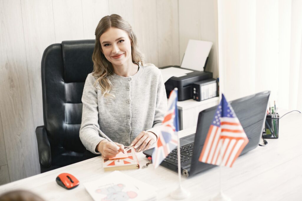 Smiling professional woman at desk with British and American flags, conveying international business.